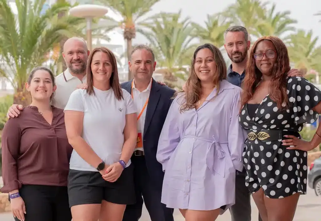 the Appco UK team smiling and standing outside in a group, with palm trees in the background
