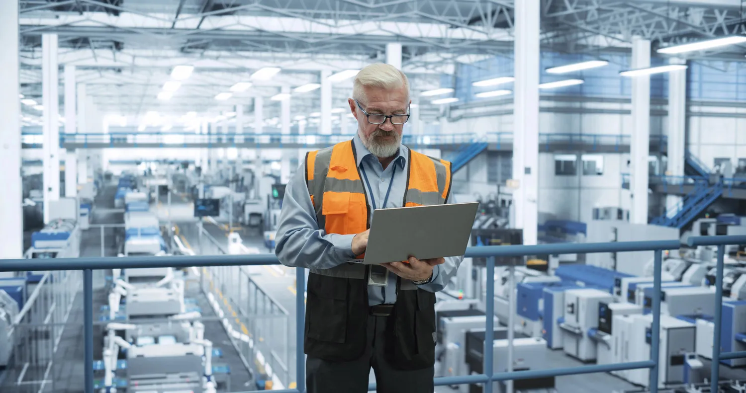 Manager using a laptop, standing above a manufacturing plant