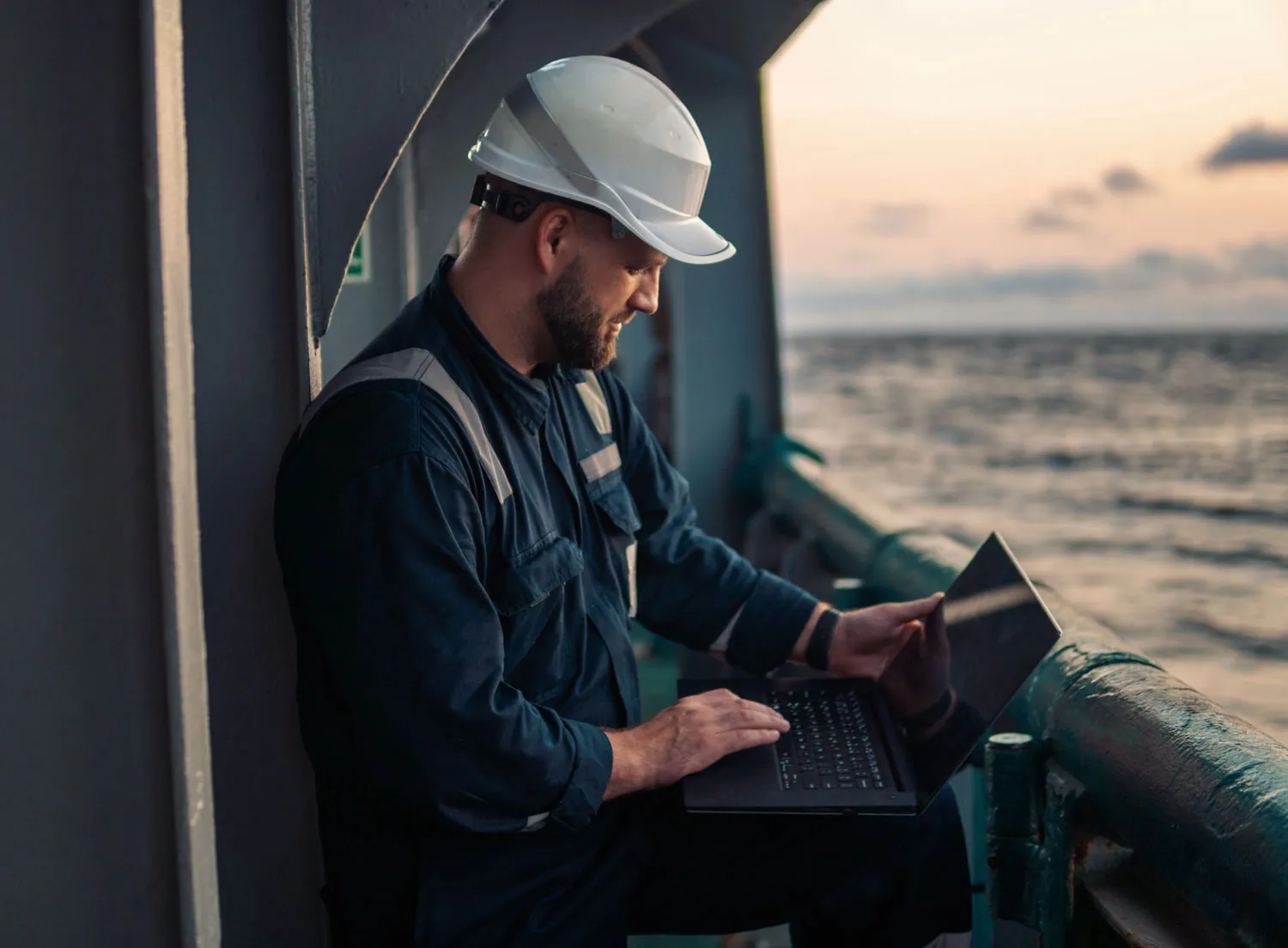 Photograph of a maritime worker using a laptop on the deck of a ship