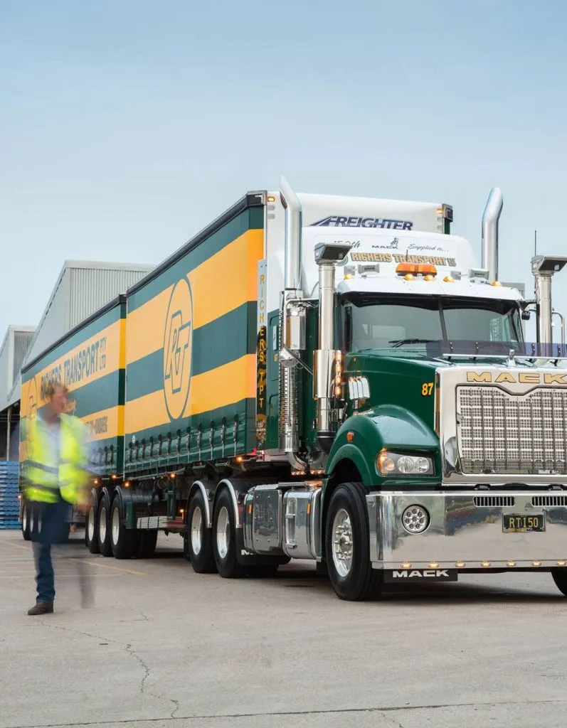 Worker in yellow high visibility vest walking away from a Richers Transport B-double truck that is painted green and yellow