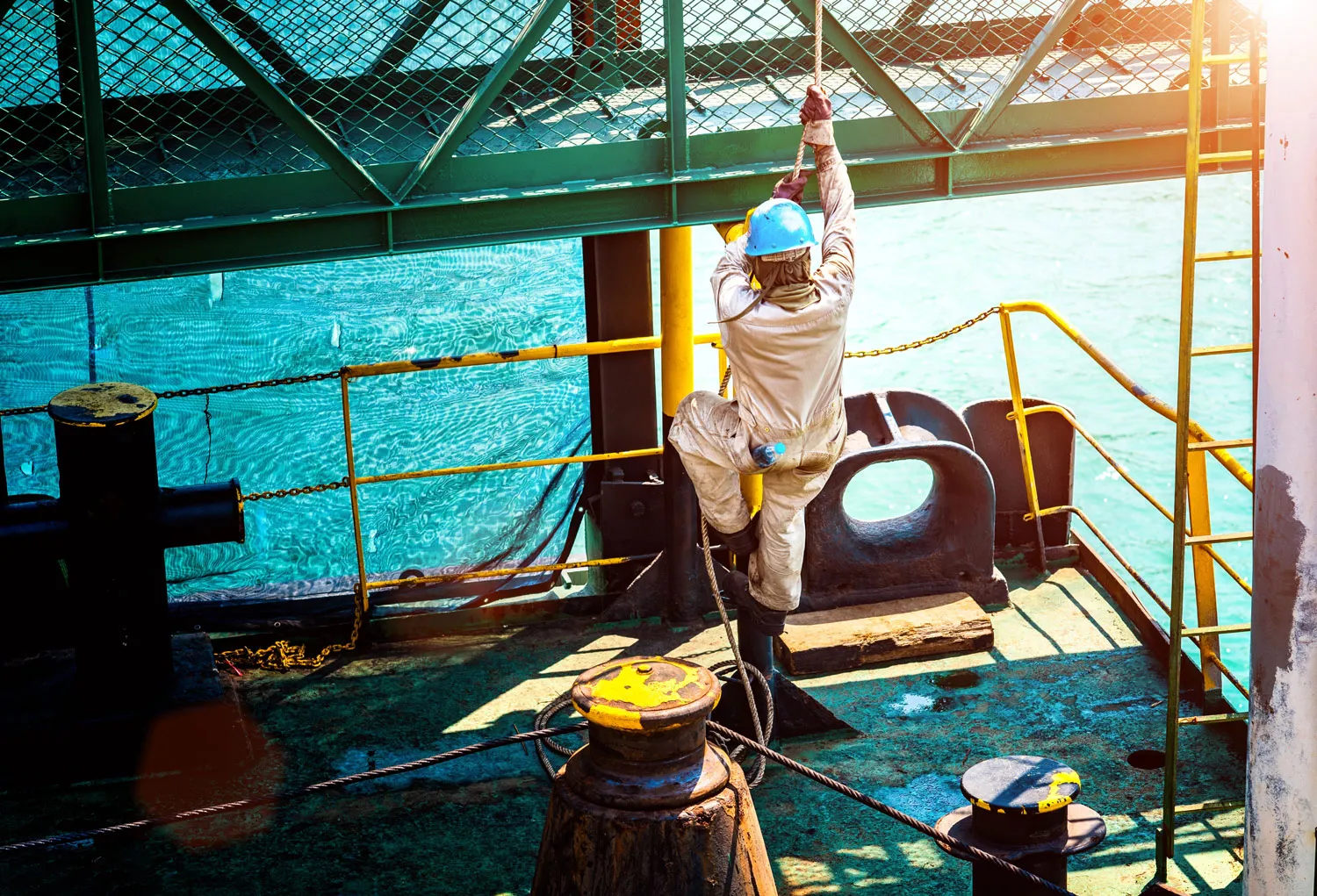 worker in a climbing harness, over a platform with ocean in the background.