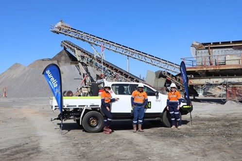 3 people in front of a truck on a mining site