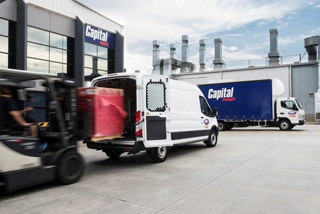 A forklift unloading goods from a white van with a blue Capital Transport Group truck in the background